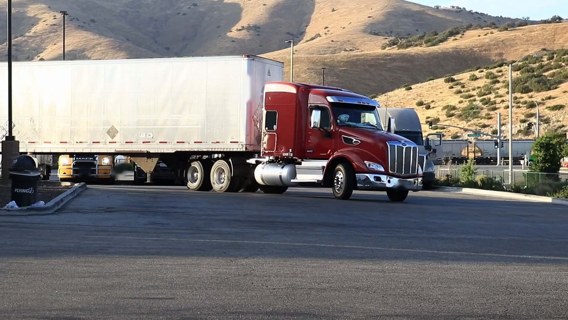 Red conventional semi-truck pulling a white trailer out onto the road at golden hour